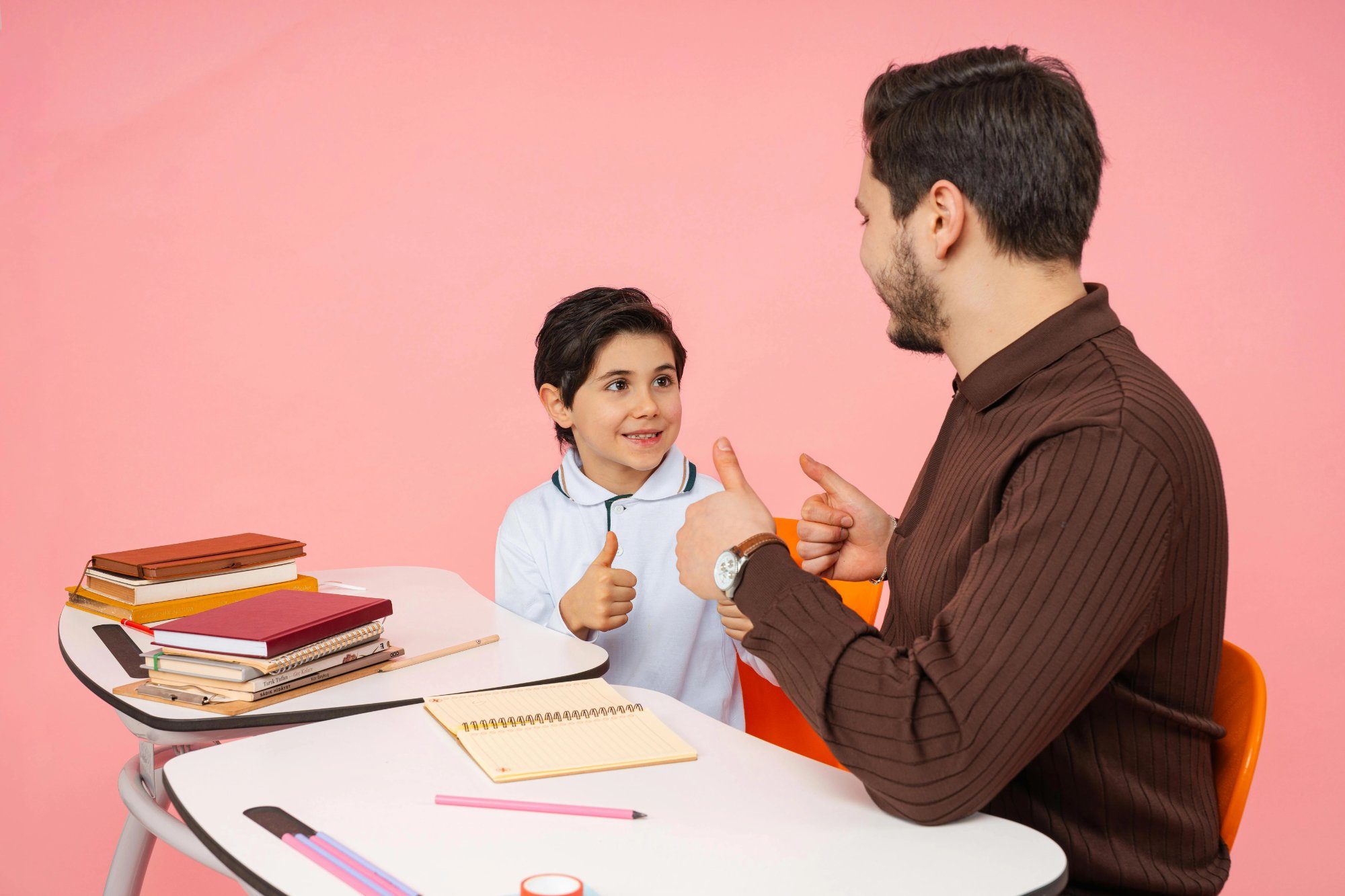 Niño y consejero adulto masculino dándose pulgares arriba en un escritorio — representando el apoyo conductual positivo y los objetivos de un plan de intervención conductual