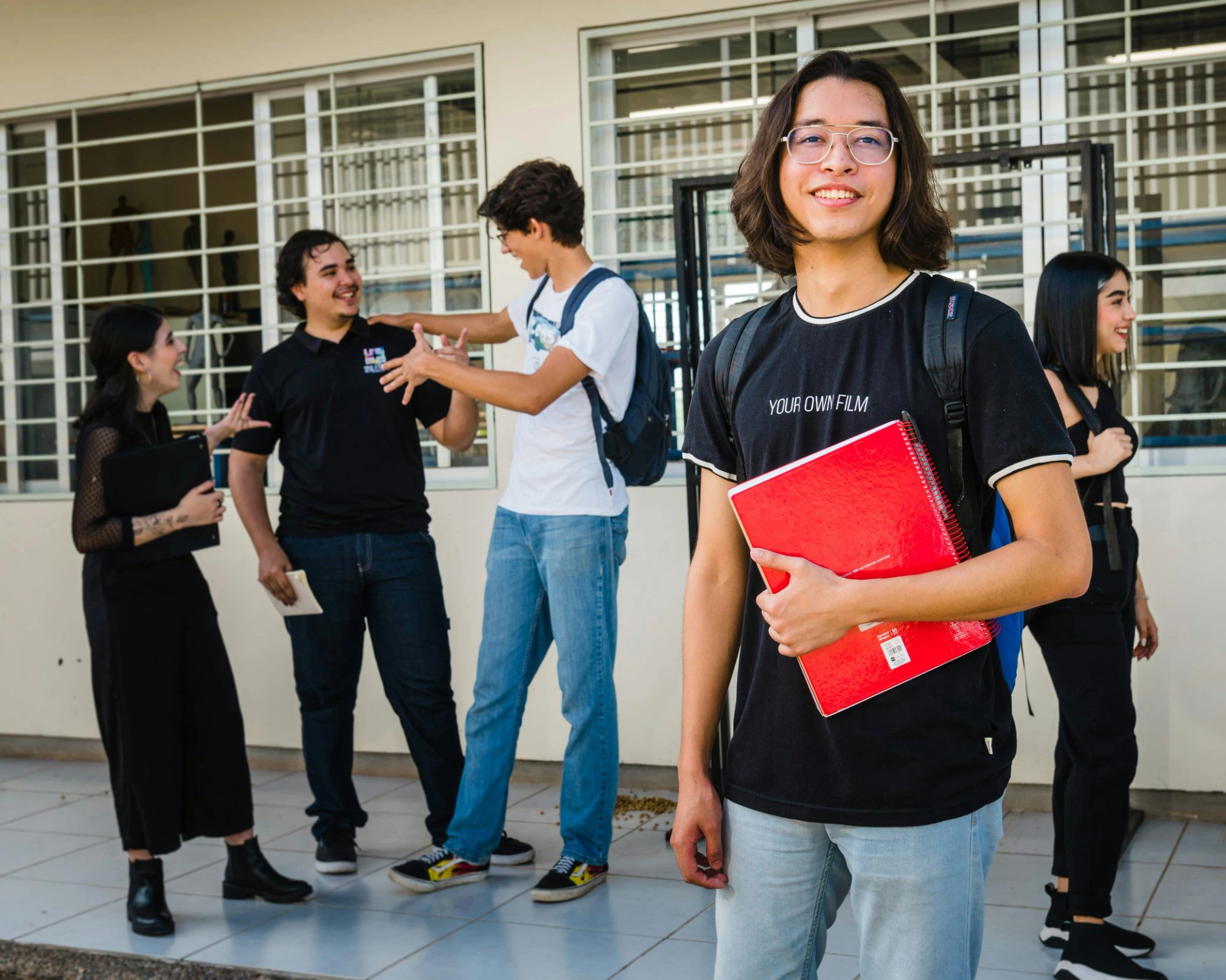 Adolescente seguro con cuaderno rojo rodeado de compañeros — representando la planificación de transición y el camino hacia la independencia